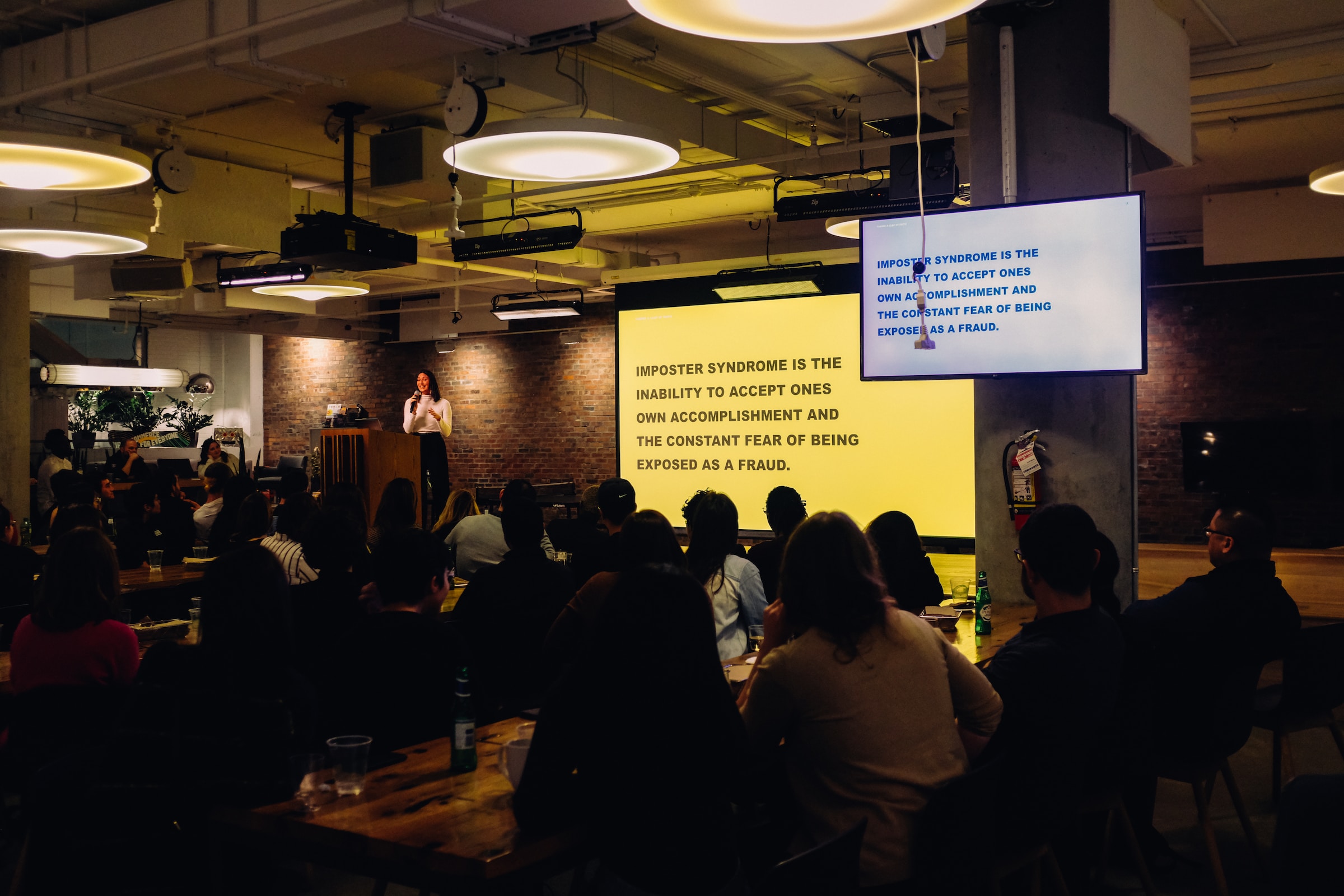 A photo of a presenter speaking to a slide about imposter syndrome - Photo by @charlesdeluvio on Unsplash (unsplash.com/@charlesdeluvio)